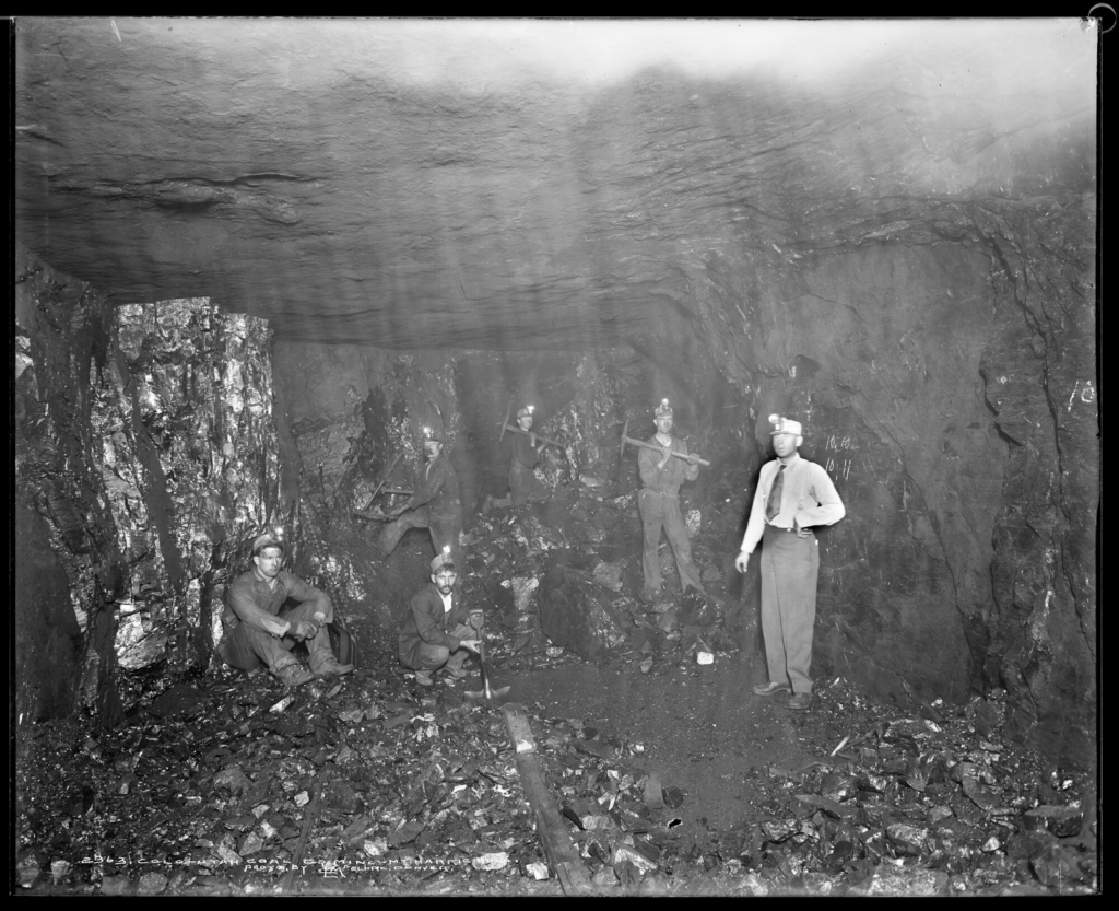 Interior view of a coal mine owned by the Colorado-Utah Coal Company at Mt. Harris, Colorado; six miners pose in the shaft holding a shovel, pickaxes and a drill.